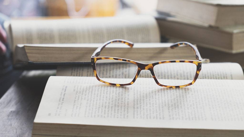 óculos colocados sobre um livro, mais livros aos fundo.