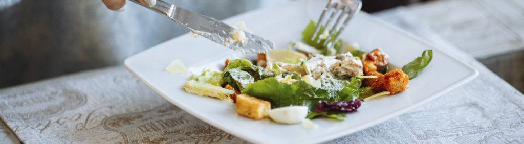 Pessoa comendo comida saudável salada verde com garfo e faca.