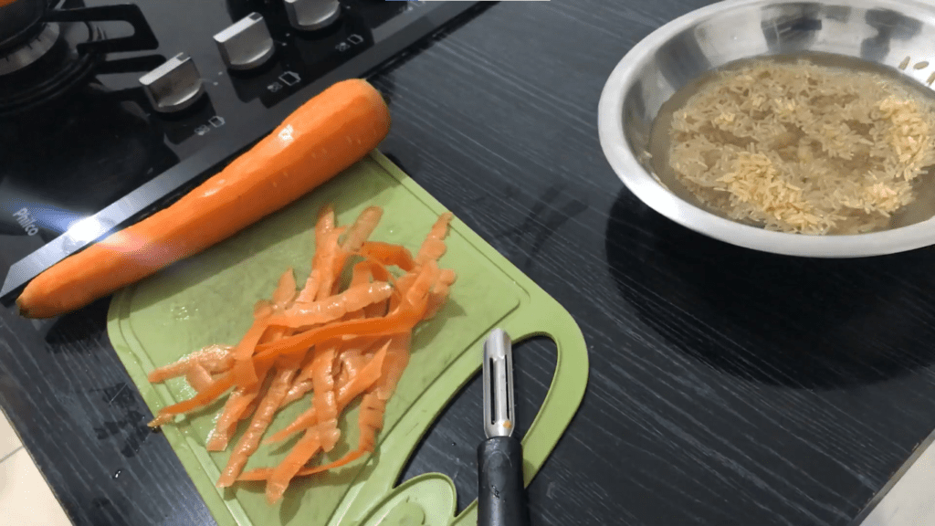 Cenoura descascado na tábua de legumes com bowl de alumínio com arroz de molho.